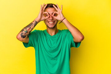 Fototapeta na wymiar Young caucasian man with tattoos isolated on yellow background showing okay sign over eyes