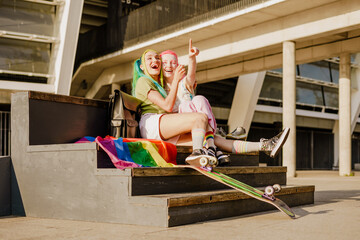 Young lesbian couple hugging and laughing while sitting at skatepark
