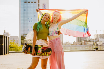 Young lesbian couple smiling and hugging while walking with rainbow flag