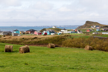 Landscape of bales of hay and small colourful traditional houses on Havre-aux-Maisons Island, with...