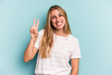Fototapeta na wymiar Young caucasian blonde woman isolated on blue background showing victory sign and smiling broadly.