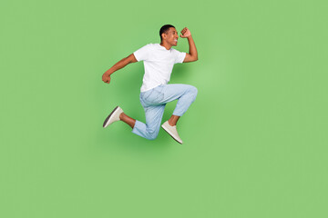 Fototapeta na wymiar Full size profile side photo of young cheerful african man runner hurry jumper look empty space isolated over green color background