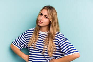 Young caucasian blonde woman isolated on blue background  frowning face in displeasure, keeps arms...
