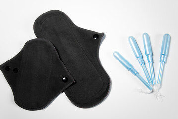 Dos compresas menstruales de algodón reutilizables junto a tampones tradicionales sobre un fondo blanco. Concepto de menstruación sostenible y sin residuos - obrazy, fototapety, plakaty