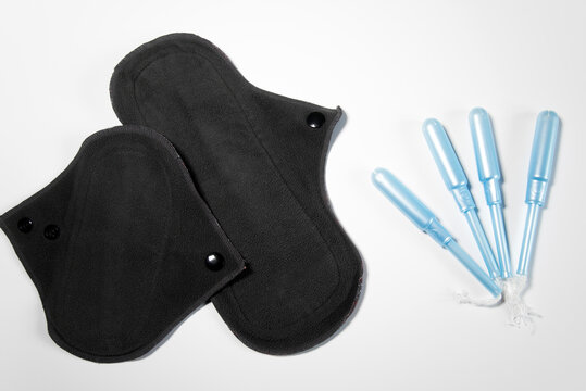 Dos compresas menstruales de algod&oacute;n reutilizables junto a tampones tradicionales sobre un fondo blanco. Concepto de menstruaci&oacute;n sostenible y sin residuos