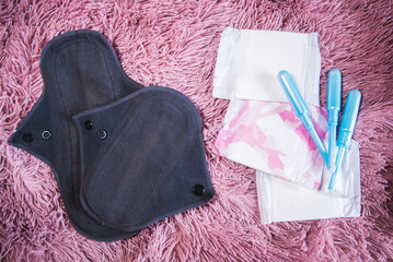 Dos compresas menstruales de algodón reutilizables junto a los tradicionales tampones y compresas sobre un fondo rosa. Concepto de períodos cero residuos - obrazy, fototapety, plakaty