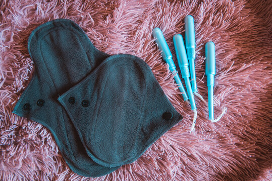 Dos compresas menstruales de algod&oacute;n reutilizables junto a tampones tradicionales sobre un fondo rosa. Concepto de menstruaci&oacute;n sostenible y sin residuos