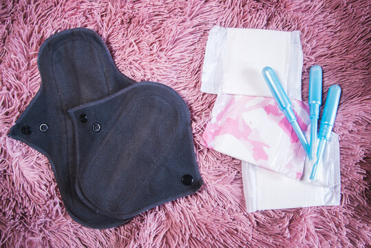 Dos compresas menstruales de algod&oacute;n reutilizables junto a los tradicionales tampones y compresas sobre un fondo rosa. Concepto de per&iacute;odos cero residuos