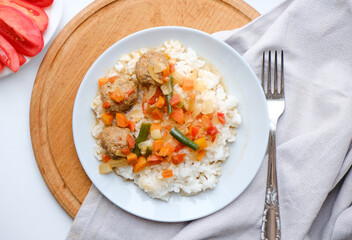 Traditional international dish. Rice with vegetable gravy and meatballs on a wooden tray and a natural gray napkin with a fork. Food template for business.