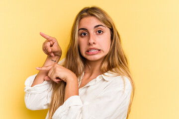 Young caucasian blonde woman isolated on yellow background  shocked pointing with index fingers to a copy space.
