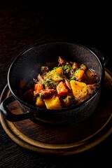 Goulash. Vegetable rague with meat, eggplant, pepper, potato and carrot in black bowl on dark wooden background