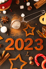 Wooden brown numbers 2023 on a dark background. There are stars carved out of wood, spices,...