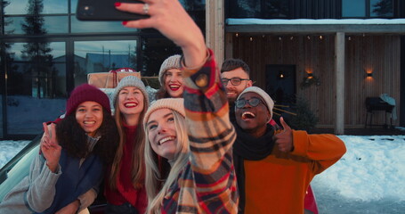 Obraz premium Group of happy multiethnic friends smile taking selfie pictures at snowy Christmas chalet house terrace slow motion.