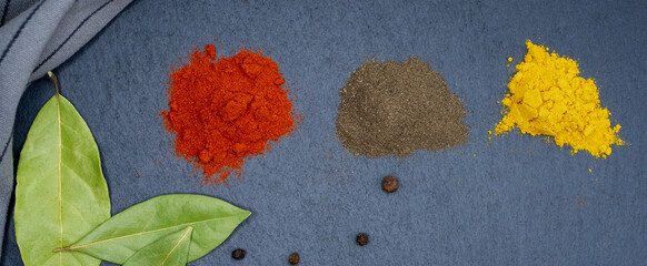 Fototapeta na wymiar Bay leaf and a pinch of turmeric, paprika, ground pepper, and a towel on a dark background.