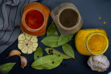 Top view. Jars of spices, bay leaf, garlic and a kitchen towel on a dark background.