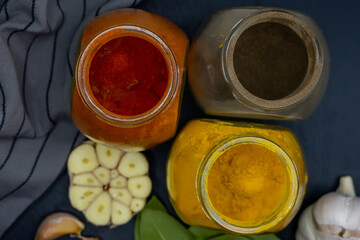 Jars with turmeric, paprika and pepper, garlic and bay leaf on a dark background. Top view.