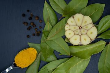 Top view of half a garlic bulb on bay leaves, pepper peas and a spoonful of turmeric on a dark...