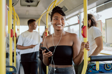 smiling woman in good mood rides bus to school in morning, headphones in ears, listening to music, drowning out conversations of passengers, holding on to railing, choice of public transport