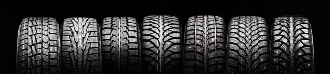 a lot of winter studded tires and velcro tires stand in a row on a black background panorama