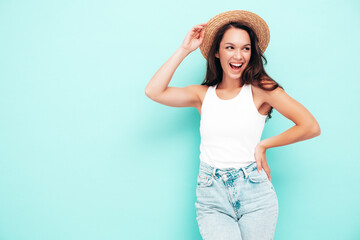 Young beautiful smiling female in trendy summer  clothes. Sexy carefree woman posing near blue wall in studio. Positive brunette model having fun. Cheerful and happy. In hat