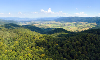 Aerial view of mountain hills covered with dense green lush woods on bright summer day