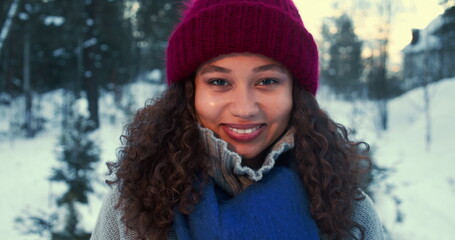 Enjoying winter. Happy young beautiful mixed race woman tying warm scarf smiling at camera at snowy forest slow motion.