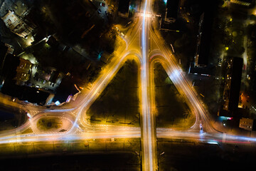 Aerial view of road intersection with fast moving heavy traffic at night. Top view of urban transportation. Rush hour with motion blurr car trail lights
