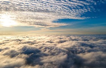 Aerial view of vibrant yellow sunrise over white dense clouds with blue sky overhead