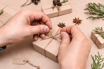 Cristmas decoration of gifts in eco-style,male hands close-up.Gift boxes are wrapped in craft paper,decorated with thuja leaves and cones.Christmas,New Year and eco-friendly concept.