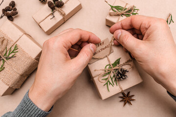 Festive decoration of gifts in eco-style,male hands close-up,top view.Gift boxes are wrapped in craft paper,decorated with thuja leaves and cones.Christmas,New Year and eco-friendly concept.