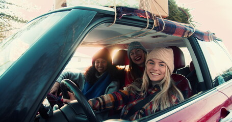 Three happy young excited multiethnic women posing, smiling at camera in fancy red car on snowy winter road slow motion. - obrazy, fototapety, plakaty