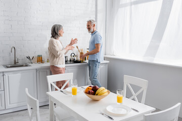 Side view of smiling mature couple talking while cooking in kitchen.