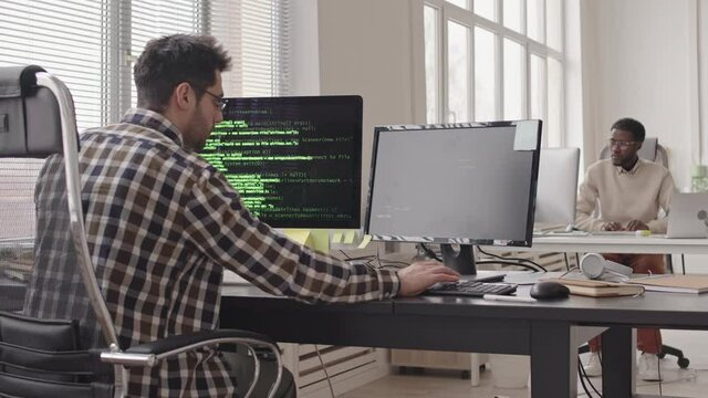 Stab shot of two young multi-ethnic male programmers working on computers in contemporary office. Running program codes on computer monitors
