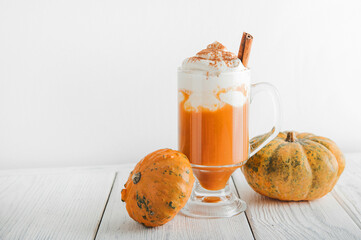 Cup with foam and cinnamon on background of pumpkins. Pumpkin autumn warming drink close-up and copy space...