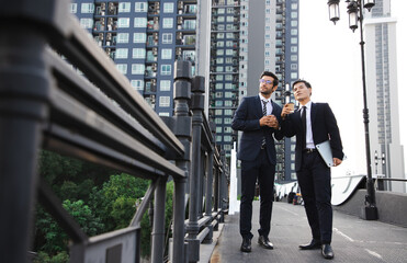 Portrait handsome businessman drink cup of coffee and work outside on bridge near cityscape and dreaming for bigger projects with business assistants outside office. Finance concept