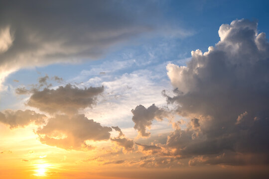 Dramatic sky at sunset with puffy clouds lit by orange setting sun © bilanol