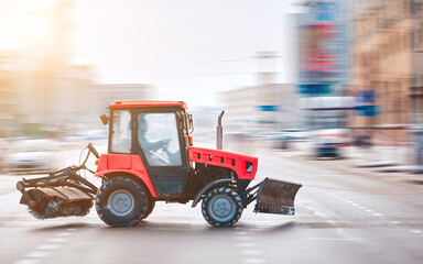 Small tractor with rotary brush and snowplough driving on city road on snowy winter day, MOTION...