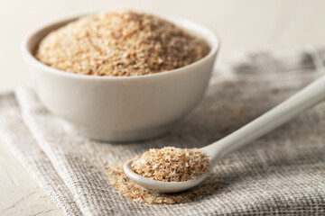 A pile of psyllium husks in a spoon and bowl on the table. Dietary supplement, superfood.
