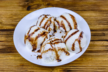 Plate with ice cream balls and chocolate topping on a wooden table