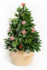 Fototapeta premium Trendy Christmas tree in wicker basket decorated red and green wooden snowflakes, natural dry flowers, eco materials isolated on white background. Creative idea for Xmas holiday. Reusable Christmas