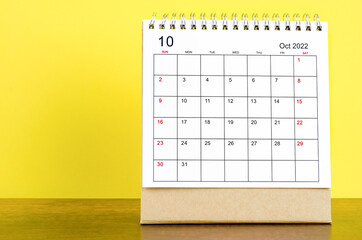 October 2022 desk calendar with yellow background on the wooden table.