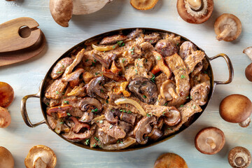 Beef stroganoff, mushroom and meat ragout with cream sauce, in a cooking pan with ingredients, overhead flat lay shot on a rustic wooden background