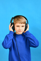 The boy listens attentively to various sounds through headphones and holds the speakers with his hands.