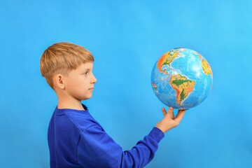 The boy holds the globe on his index finger and looks at it.