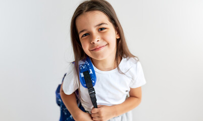 Cute schoolgirl smiling wearing white t-shirt with blue backpack looking at the camera posing against white background. Positive schoolkid with backpack has joyful expression to going back to school.