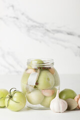 Green tomatoes for canning in a glass jar on a light background. Unripe tomatoes for harvest.