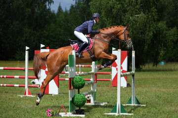 Young equestrian girl jumps obstacle with bay horse in show jumping