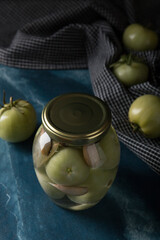 Green tomatoes for canning in a glass jar on a blue marble background. Unripe tomatoes for harvest.