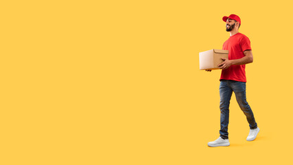 Fototapeta premium Arabic Male Courier Carrying Parcel Box Walking Over Yellow Background