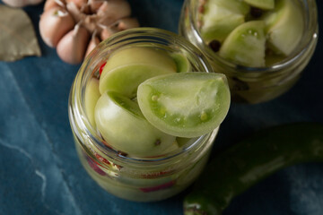Green tomatoes for canning in a glass jar on a blue marble background. Unripe tomatoes for harvest.